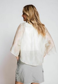 Lightweight, sheer white blouse with wide sleeves and a patterned overlay, paired with a gray cargo skirt with pockets.