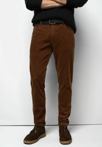 Brown corduroy pants with a slim fit, featuring a textured surface and front pockets, paired with dark brown suede ankle boots.