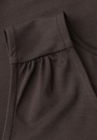 Tissu brun foncé en gros plan montrant des plis froncés près d'une couture de poignet pliée sur un vêtement en maille.