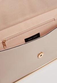 Kovově béžová kabelka s hladkým povrchem, vybavená zlatým kováním a zapínáním na druk, s růžovou podšívkou a kapsou na zip.