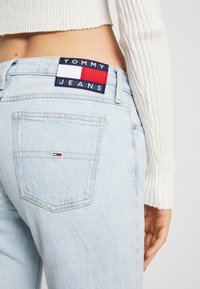 Světle modré denimové džíny s vysokým pasem, s kontrastní tmavě modrou nášivkou na pase označenou "TOMMY JEANS" a malým logem na zadní kapse.