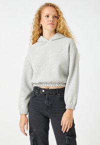 Sudadera gris corta con capucha ajustable, cinturilla elástica y mangas largas. Combinada con pantalones cargo negros que tienen bolsillos laterales.