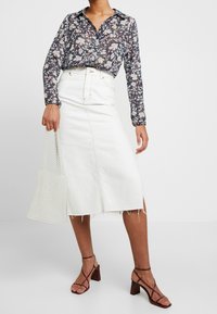 Blommig blus med långa ärmar i mörkblått med ljusa blommor, matchad med en vit denimkjol med en framåtsydd söm och rå fåll.