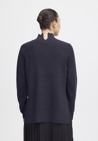 Dunkelblauer gestrickter Pullover mit hohem Kragen und einer Rückenschnitze. Lange Ärmel und lockerer Schnitt. Rippbündchen an Saum und Ärmeln.