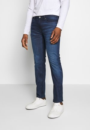 Donkerblauwe spijkerbroek met een slim fit, voorzien van een klassieke vijf-pocketontwerp en subtiele vervaging. Gecombineerd met witte sneakers.