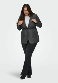 Uhlově šedý blazer s páskem v pase, doplněný černými rozšířenými kalhotami. Blazer má dvě přední kapsy a klopový límec.
