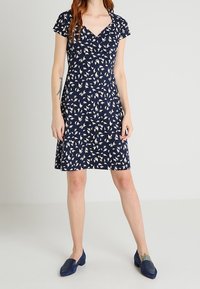 Navy blue dress with a v-neck and cap sleeves, featuring a white leaf pattern. Model pairs with dark blue textured flats.