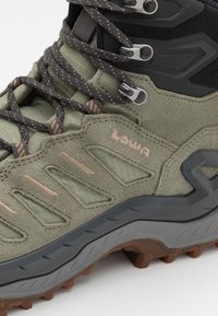 Scarpa da trekking in suede verde oliva e tessuto, con suola in gomma grigia, dettagli in rete, lacci multicolori e logo impresso sul lato.