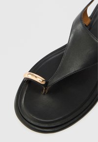 Czarne skórzane sandały na ramiączku o gładkiej fakturze, z błyszczącym złotym akcentem na pasku oraz płaską podeszwą.