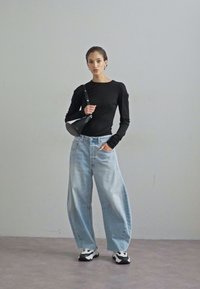 Svart langermet topp, lyseblå baggy jeans og svart-hvite joggesko. Tilbehøret inkluderer en liten svart skulderveske.