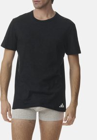 Black crew neck t-shirt made of smooth cotton, with short sleeves and a small white logo accent on the lower right side.