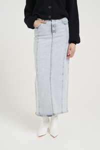 Lys blå denim maxi skjørt med vertikal søm, frontlomme og en kant som når ankelen, paret med hvite spisse støvler.