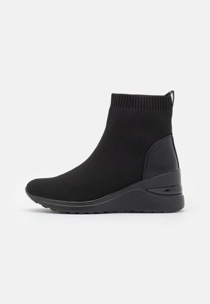 Bottes cheville en maille noire avec une tige texturée, un talon compensé en néoprène et un accent lisse à l'arrière, conçues pour le confort.