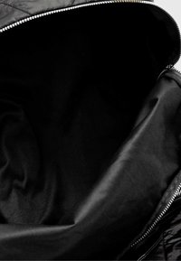 Interno di un bag nero con zip, caratterizzato da un tessuto liscio con una leggera lucentezza, senza modelli o scompartimenti visibili.