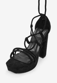 Sandalia de tacón alto de ante negro con punta cuadrada, múltiples correas entrelazadas y un tacón grueso. Forro interior suave. Talla 36.
