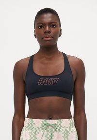 Morska sportska grudnjak s logotipom "ROXY" u crvenoj boji. Ima klasičan dizajn s širokim trakama i glatkom površinom. Uparen s kratkim hlačama s uzorkom.