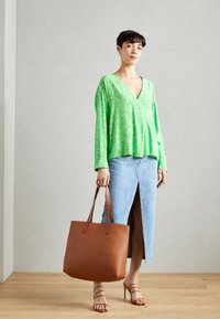Grønn langermet topp med blomsterdesign, denimskjørt med frontslitt, brun skinn tote bag og nude høyhælte sandaler.