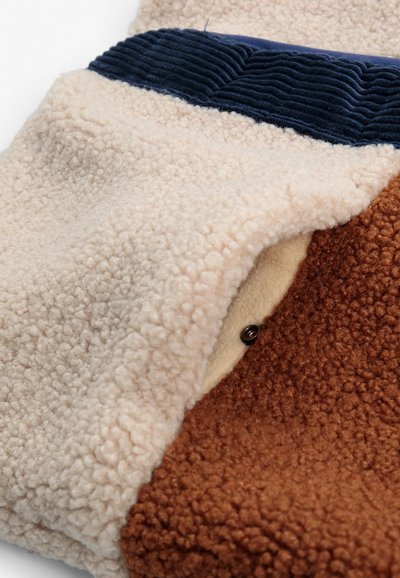 Tissu polaire doux en crème, marron et marine avec un bouton-pression visible et une bordure côtelée texturée sur la partie marine.