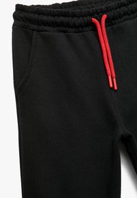 Sorte sweatpants med elastisk talje og røde snore. Har to sidelommer og et blødt, tekstureret stof.