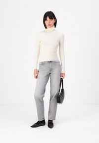 Bijela rebrasta turtleneck džemper, svijetlosive ravne traperice, crna torba s zakovicama i crne cipele s oštrim vrhom. Glatke teksture, ležeran kroj.