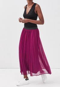 Débardeur noir sans manches associé à une longue jupe plissée en tulle magenta. La jupe est dotée d'une taille élastique et est portée avec des baskets blanches.