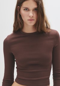 Braunes, langärmliges, eng anliegendes Oberteil aus glattem Stoff. Verfügt über einen Rundhalsausschnitt und ein kurzes Design mit minimalen Nähten.