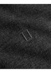 Un material textil tricotat de culoare neagră, cu o suprafață texturată, având un mic, subtil „II” brodat în colțul de jos, de culoare gri.