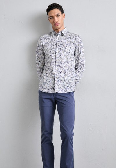 Camicia button-up con motivo floreale blu e viola su uno sfondo chiaro, abbinata a pantaloni blu navy, dalla texture morbida.