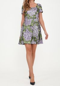 Blommönstrad klänning med lila blommor och gröna blad på en ljus bakgrund. Korta ärmar och en åtsittande midja som leder till en utsvängd kjol.