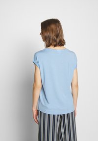 Jasnoniebieska koszula z krótkim rękawem z miękkiego materiału, ma okrągły dekolt i luźny krój, zestawiona z pasiastymi spodniami, tworzy swobodny look.