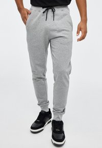 Pantalones de chándal grises con un diseño de pierna ajustada, fabricados en tejido suave, con una cinturilla elástica con cordón y bolsillos laterales.