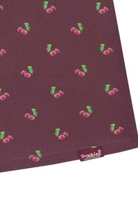 Tissu bordeaux avec un motif de cerises répétitif, comportant des feuilles vertes. Petite étiquette en tissu dans le coin inférieur indique "Pockies Couch Couture."