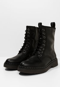 Zwarte leren enkelboots met een vetersluiting aan de voorkant, zijrits, stevige zool en gestopte accenten langs de basis. Textuurafwerking aan de bovenkant.