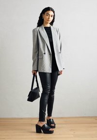 Hallgrey ja valge triibuline bleiser kahe nupuga, koos musta topi ja vormikate mustade nahkpükstega. Mustad platvormkingad ja väike kott.