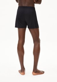 Shorts de bain noirs avec une ceinture élastique, longueur au-dessus du genou et finition textile lisse, vus de dos.