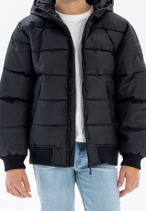 Doudoune noire à capuche, avec un design matelassé, fermeture éclair à l'avant et poignets élastiques. Associée à un t-shirt blanc uni et un jean bleu clair.