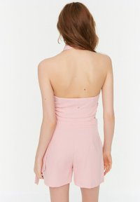 Różowy kombinezon na szyję z dopasowanym gorsetem, marszczonymi detalami oraz szortami z bocznymi kieszeniami. Gładka tkanina o lekkiej teksturze.