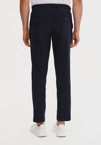 Granatowe spodnie o prostym kroju, wykonane z fakturowanej tkaniny, z dwoma tylnymi kieszeniami i mankietami, zestawione z białymi sneakersami.