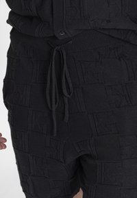 Pantaloni corti neri in maglia con un motivo logo in rilievo, vita con cordino e tasche laterali, realizzati in un tessuto strutturato per un dettaglio aggiuntivo.