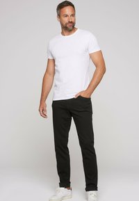 T-shirt bianca a colletto rotondo abbinata a pantaloni neri aderenti e sneakers bianche. L'outfit è semplice, con un design casual e colori classici.