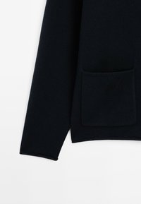 Navy blue knitted sweater with long sleeves, featuring a rectangular front pocket and ribbed cuffs. Soft texture and clean lines.