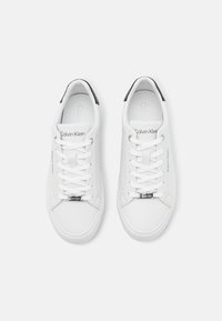 Baskets en cuir blanc à finition lisse, avec des accents noirs au talon, des lacets blancs et un logo argenté sur le côté et la languette.