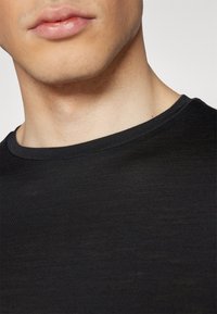 Camiseta de algodón negra con un cuello redondo, textura fina y acabado suave, mostrando el cuello y parte de la zona del pecho superior.