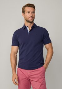 Polo shirt blu navy con bottoni e colletto a contrasto con motivo, abbinato a pantaloni corti rosa. Mischia di cotone, texture liscia.