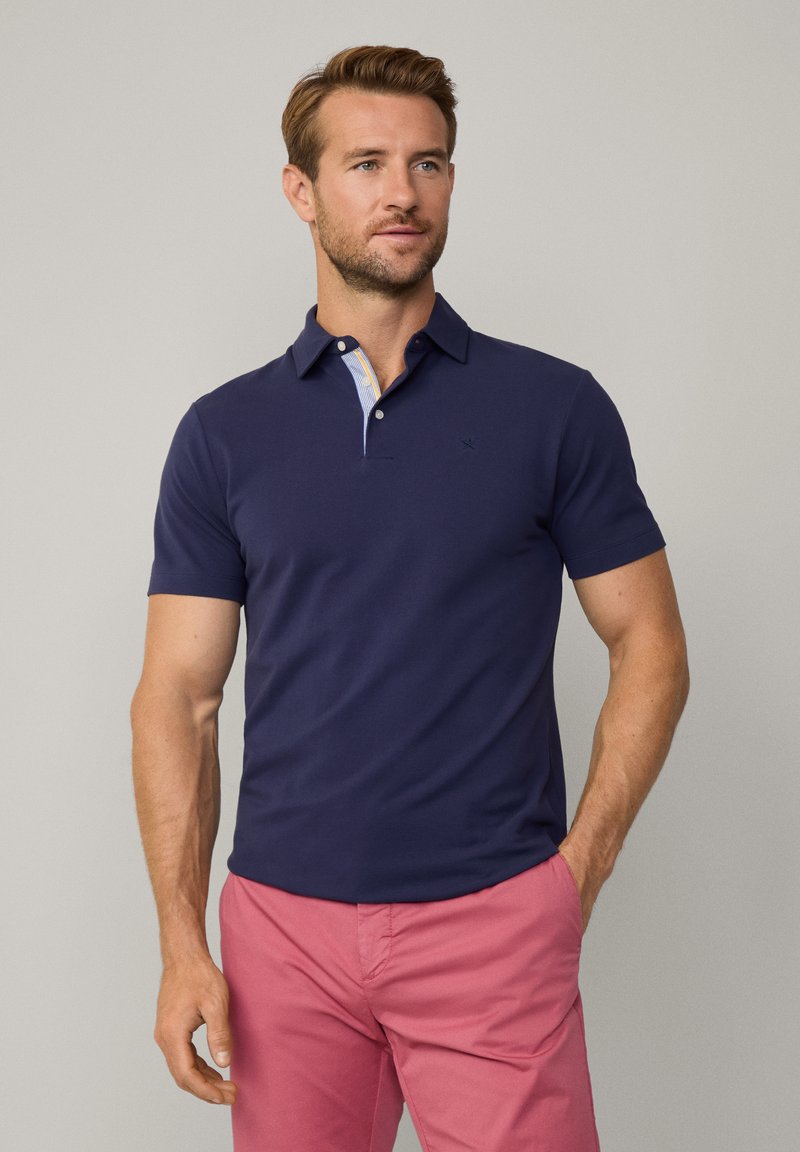 Polo shirt blu navy con bottoni e colletto a contrasto con motivo, abbinato a pantaloni corti rosa. Mischia di cotone, texture liscia.