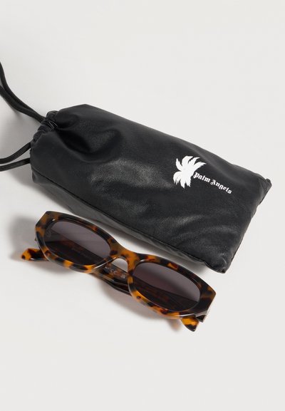 Lunettes de soleil rectangulaires en écaille avec des verres foncés à côté d'une pochette noire à cordon avec un logo de palmier blanc et le texte "Palm Angels".