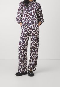 Completo stampato composto da due pezzi, con una maglietta a maniche lunghe e scollatura arricciata, e pantaloni a gamba larga in bianco, viola e blu con schemi astratti.