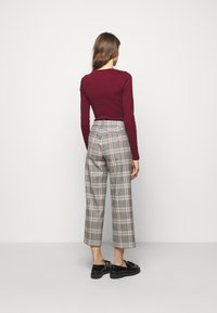 Mörkröd långärmad topp som kombineras med grårutiga vida byxor; byxorna har subtila inslag av beige och röd, samt fickor. Svarta skor fulländar looken.