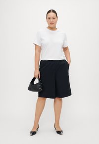 White short-sleeve t-shirt, black elastic waist shorts, black handbag with silver accents, sleek black pointed-toe shoes.