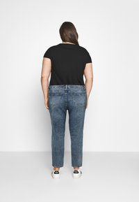 Camisa negra de manga corta combinada con jeans de cintura alta azules y zapatillas blancas. Los jeans presentan un diseño clásico de cinco bolsillos.